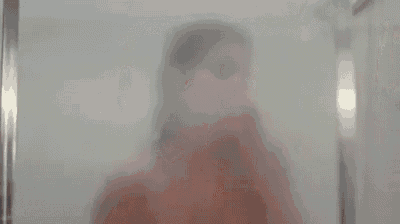 a woman is taking a shower with soap on her face and looking at the camera .