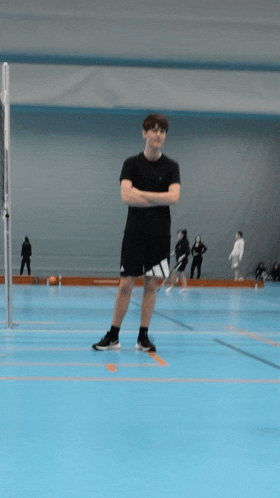 a young man stands with his arms crossed on a blue court