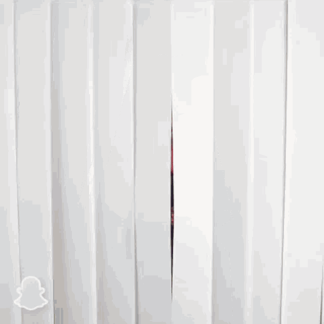 a man wearing glasses and a bandana is peeking out from behind a white curtain