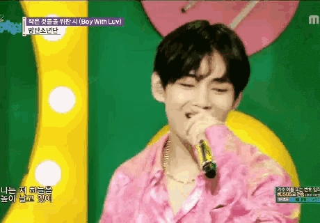 a man in a pink shirt is singing into a microphone with the words boy with luv above him