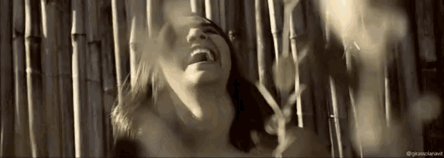 a woman is laughing in front of a fence made of bamboo