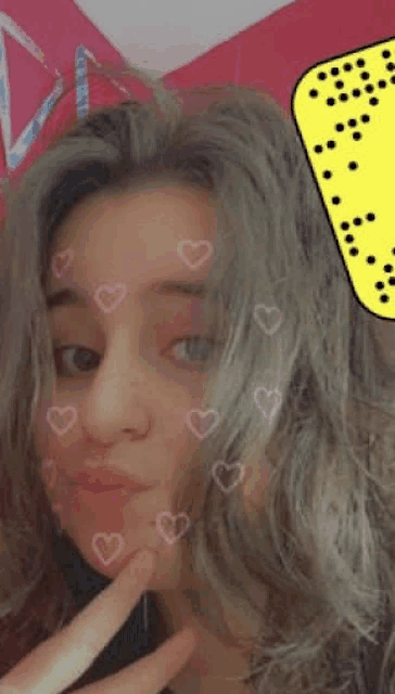 a girl with hearts on her face is taking a selfie with her finger in her mouth .