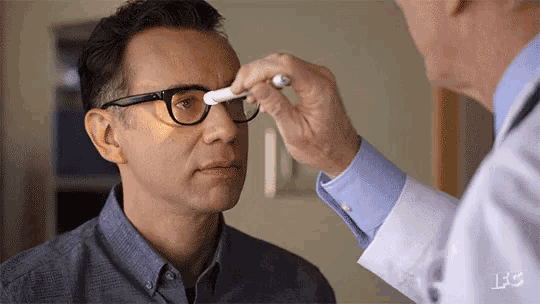 a man with glasses is getting his eyes examined by a doctor