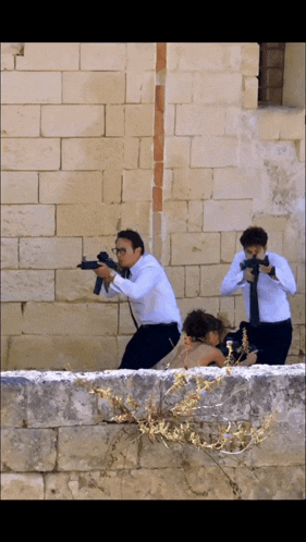 a man in a white shirt and tie is holding a gun in front of a brick wall