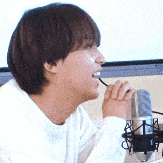 a man in a white shirt is sitting in front of a microphone with a pen in his mouth
