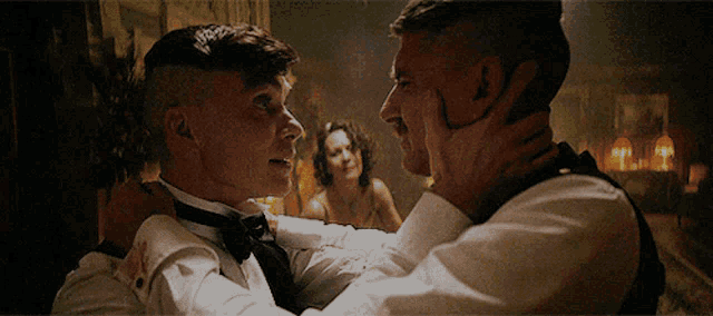 a man in a tuxedo is holding another man 's face in a dark room
