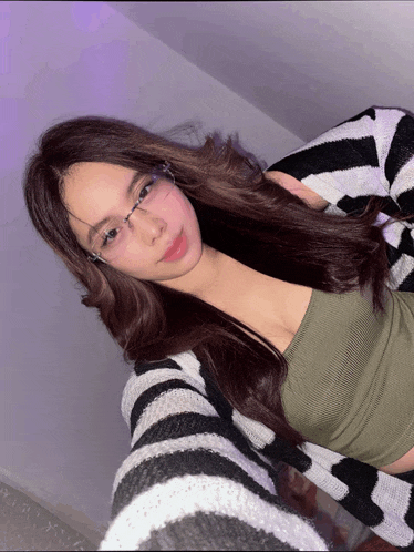 a woman wearing glasses and a striped sweater is taking a selfie