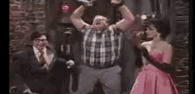 a man in a plaid shirt is jumping in the air while a woman in a pink dress looks on .
