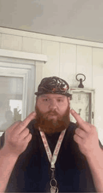 a man with a beard and hat is giving the middle finger in front of a clock .