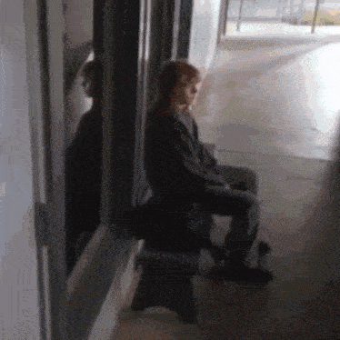 a person is sitting on a bench in a hallway looking out a window