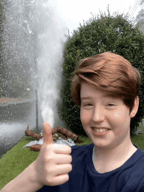 a young boy is giving a thumbs up in front of a water jet