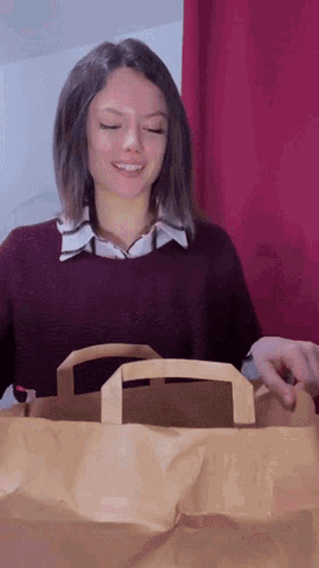 a woman in a purple sweater is holding a brown bag
