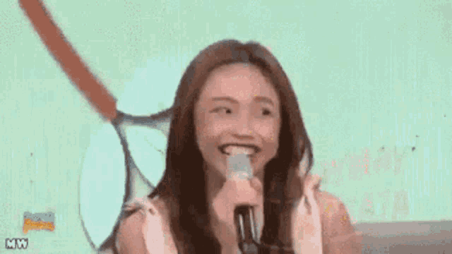 a woman is holding a microphone in front of a tennis racquet and the words maymay entrata on the bottom