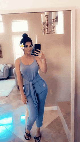 a woman in a blue jumpsuit is taking a selfie in front of a mirror .