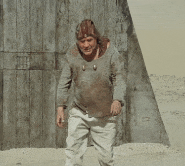 a man wearing a helmet and a dirty shirt is standing in the sand .