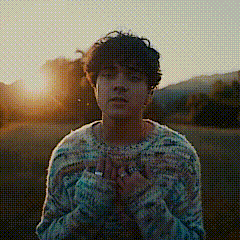 a man in a sweater is standing in a field at sunset .