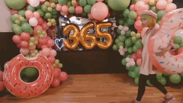 a woman walking in front of a wall of balloons with the number 365 on it