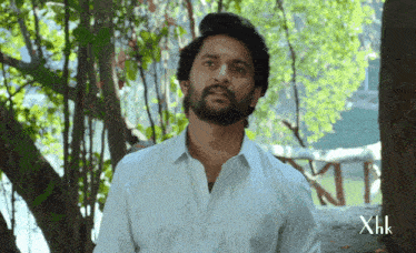 a man with a beard wearing a white shirt with the letters xhk on the bottom right