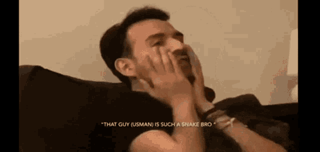 a man is laying on a couch covering his face with his hands and laughing .