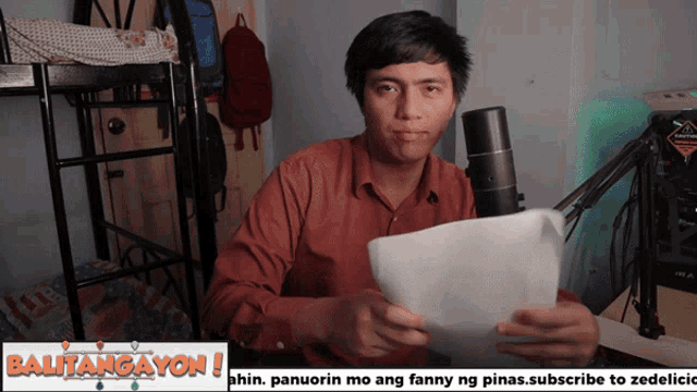 a man is holding a piece of paper in front of a microphone with the words balitangayon written on the bottom