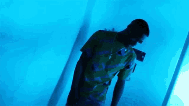 a man in a colorful shirt is standing in a blue room with a shadow behind him .