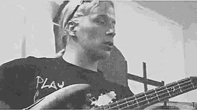 a man in a black shirt is playing a bass guitar in a black and white photo .