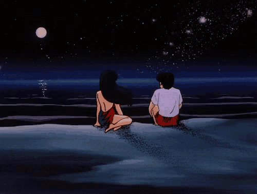 a man and a woman are sitting on the beach at night looking at the moon