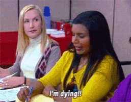 a woman in a yellow sweater says i 'm dying while sitting at a desk
