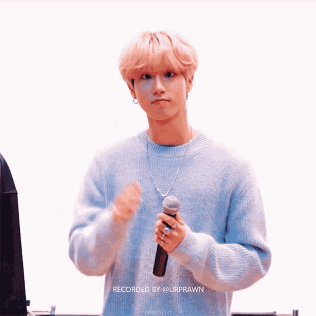 a young man in a blue sweater is holding a microphone and has the words recorded by @urprawn written below him
