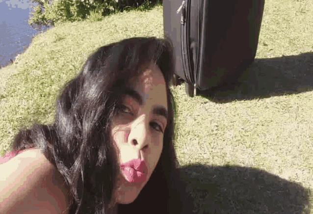 a woman laying on the grass with a suitcase behind her
