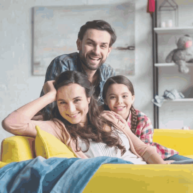 a family sits on a yellow couch and smiles at the camera