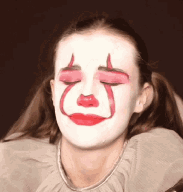 a young girl has her face painted like a clown and has her eyes closed .
