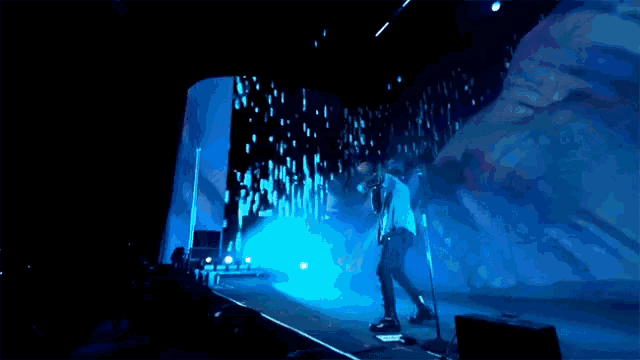 a man singing into a microphone on a stage with a large screen behind him