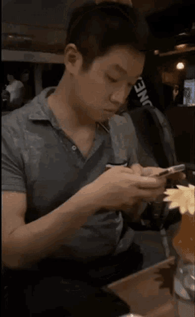 a man is sitting at a table looking at his phone with a sign behind him that says ' xinex '