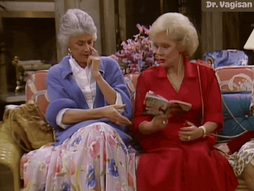two women are sitting on a couch and one of them is reading a book