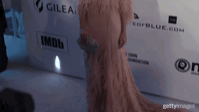 a woman in a long pink dress is standing in front of a wall that says imdb