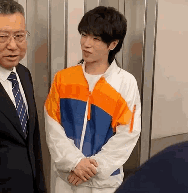 a man in a suit and tie is shaking hands with a young man wearing a jacket .