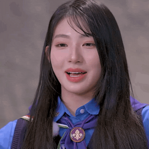 a girl wearing a blue shirt and a purple tie with a fleur de lis badge