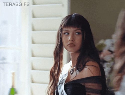 a woman with long hair and bangs is standing in front of a window with the words terasgifs on the bottom right