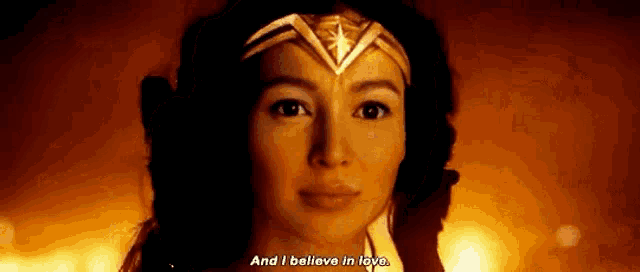 a woman in a wonder woman costume is standing in front of a fire and saying `` and i believe in love . ''
