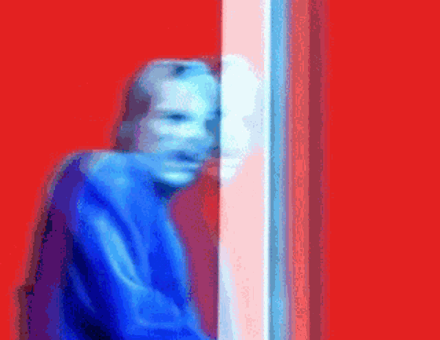 a blurry picture of a man in a blue sweater standing in front of a red wall