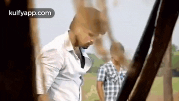 a man in a white shirt is standing in a field next to another man in a plaid shirt .