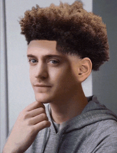 a young man with curly hair is wearing a grey sweatshirt
