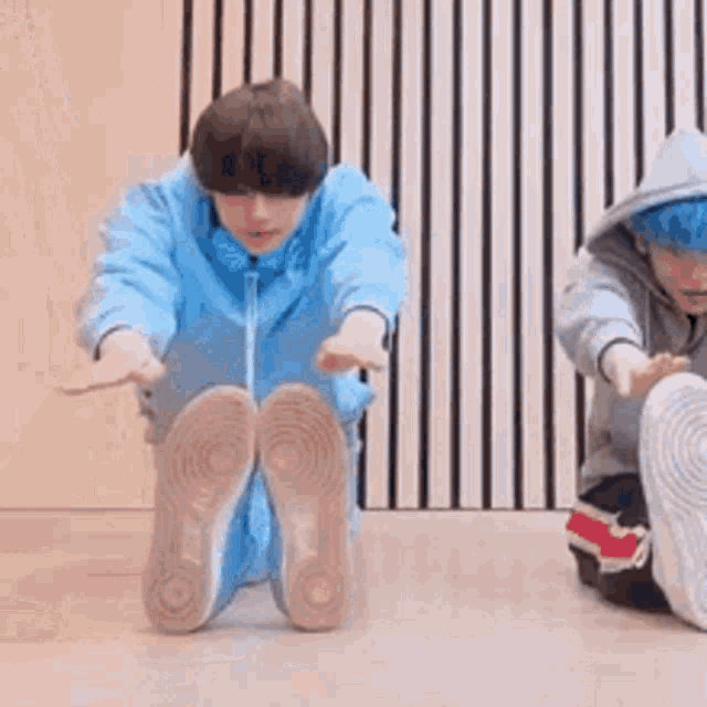 two young boys are sitting on the floor stretching their legs .
