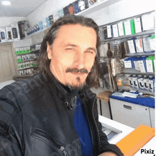 a man with long hair and a beard is wearing a leather jacket and a blue shirt