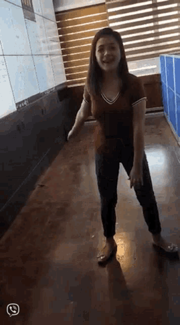 a woman in a red shirt and jeans is standing on a wooden floor .