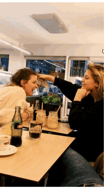 two women sitting at a table with a bottle of diet coke on it