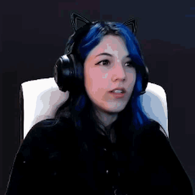 a girl with blue hair and cat ears is wearing headphones and sitting in a chair .