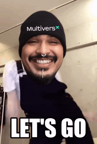 a man wearing a hat that says " multivers " is smiling and says " let 's go "