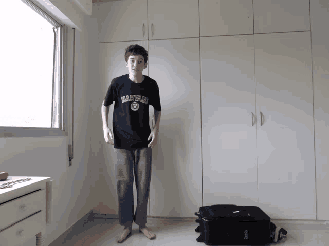 a young man wearing a shirt that says harvard stands in a room